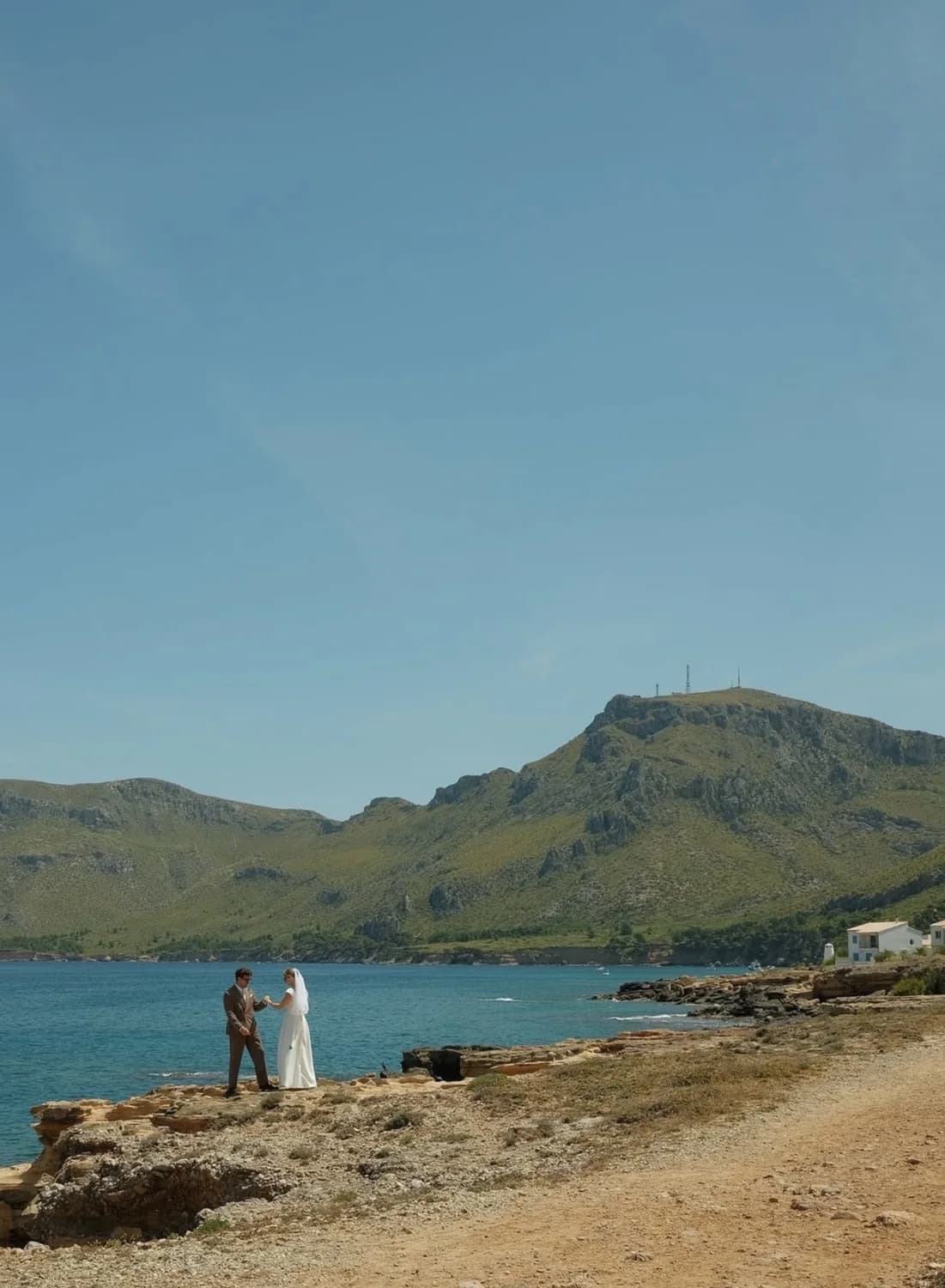 Brudparet håller varandras händer på klipporna vid havet