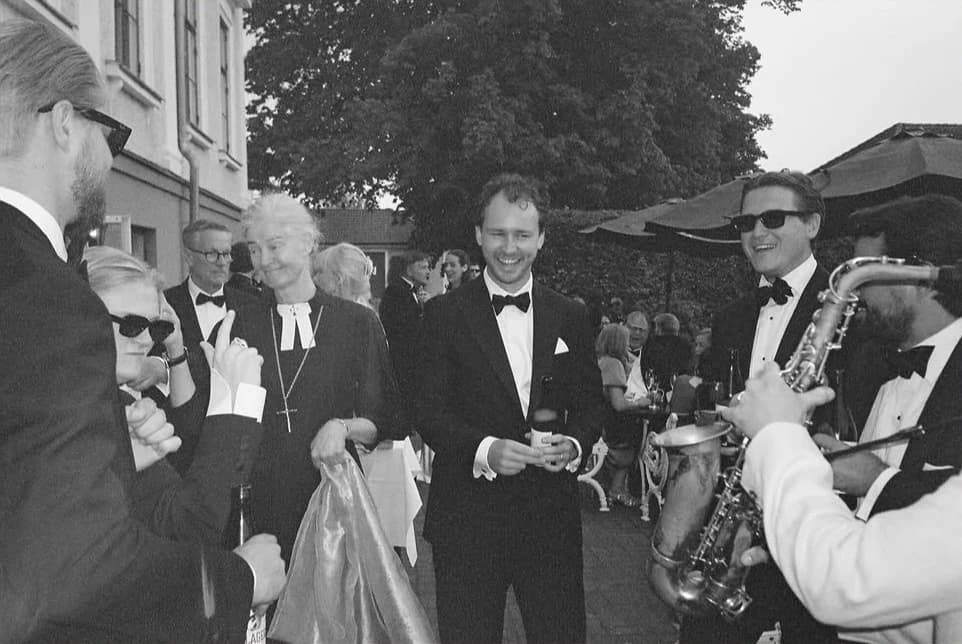 Skratt och saxofon bland gästerna utanför festen, i svartvitt
